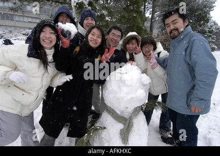 group of happy chinese students having fun with snowman Aberystwyth University, in the snow,  Ceredigion Wales UK Stock Photo