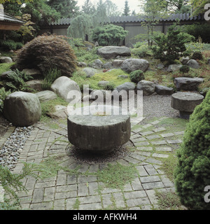 Old Stone Mill Wheel In Paved Area Of Japanese Style Garden With Large Rocks And Small Conifers And Acer Tree Stock Photo Alamy