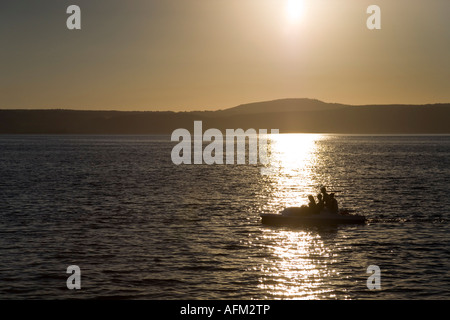 Small pedal boat with people on Bracciano lake near Anguillara Sabazia at dusk with hills and setting Sun background Stock Photo