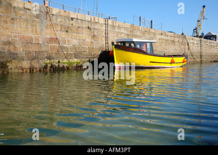 A colourful yellow boat moored in the harbour at Penzance, Cornwall, UK with nice reflections on the water. Stock Photo