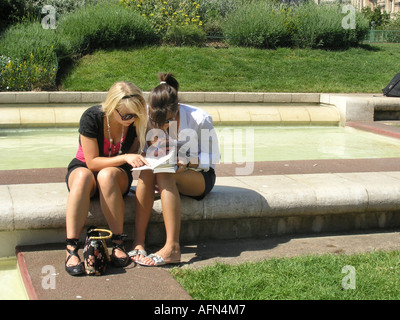 two young women looking at guide book of Paris planning their day Jardin du Forum des  Halles Paris France Stock Photo