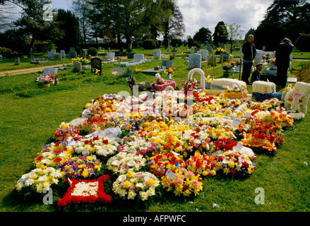 Gypsy grave traditional gypsies horse and wagon.  Wreaths,  numerous floral tributes. Gravedigger and two family members chatting. Hampshire England Stock Photo
