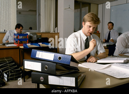 Civil Servants office work 1990s UK Group men at their desks in office. Jackets off in their shirt sleeves. Folders on desk sucking on a biro London. Stock Photo