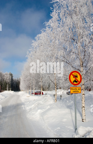 Walkway , birch trees covered with with frost , clear blue sky and Finnish traffic sign ( No entry for power-driven vehicles ) , Finland Stock Photo