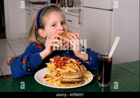 Junk food unhealthy overeating teen young schoolgirl eating a huge hamburger and chips drinking coke at home in after school London HOMER SYKES Stock Photo