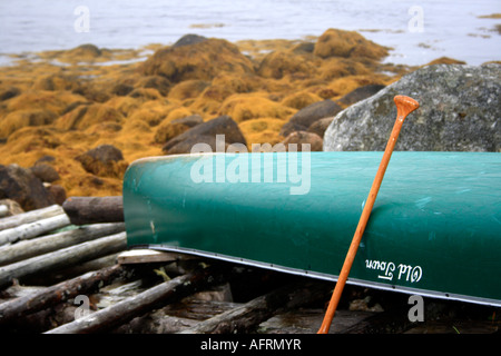 Old Town canoe lying upside down with wooden paddle on riverside boat ramp, Nova Scotia, Canada. Photo by Willy Matheisl Stock Photo