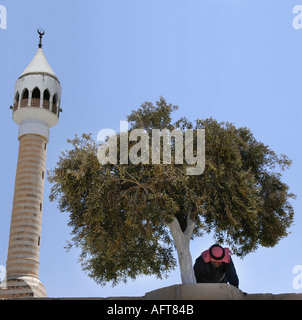 A Muslim man praying in front of a Mosque under an olive tree in the direction of Mecca in the town of Salt Jordan Stock Photo