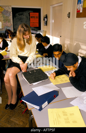Secondary School 1990s UK. Teacher sitting on desk, one asian student helps a Sikh student friend. Greenford High School, Middlesex London 1990. Stock Photo