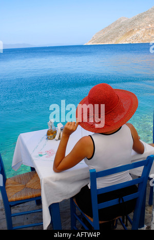 Woman sitting at a restaurant table on the waterfront of the island town of Symi Greece Stock Photo