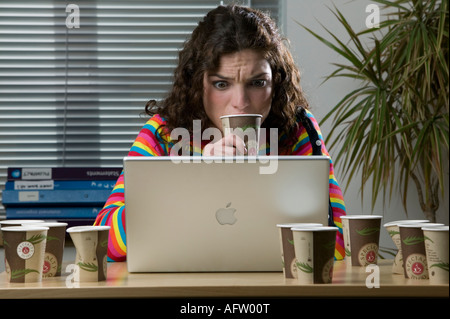 A very frustrated female office worker looking into a laptop screen surrounded by paper coffee cups Stock Photo