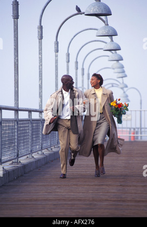 An African American couple run arm in arm on a dock Stock Photo