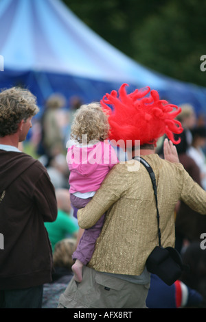 A dad wearing a red wig holds up his child to see a performance at the Big Chill music Festival August 2007 Stock Photo