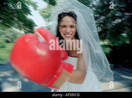 Bride play fighting in her wedding dress and veil wearing boxing gloves Stock Photo