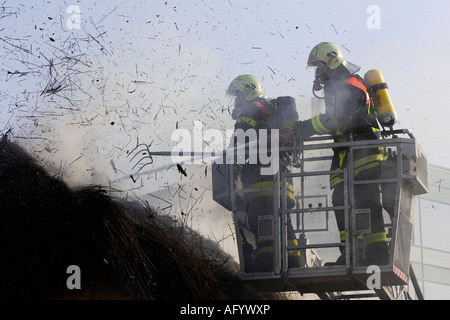 Firemen extinguish fire on a thatched roof Stock Photo