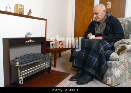 A elderly man sitting infront of his unlit electric fire Stock Photo