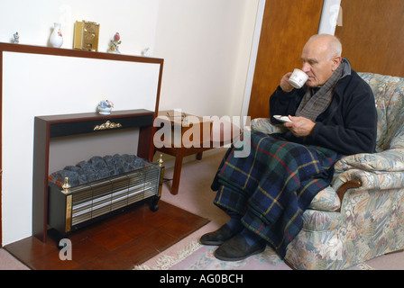 A elderly man sitting infront of his unlit electric fire Stock Photo