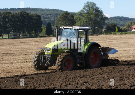 Green Claas tractor towing mounted plough (stubble ploughing, turning soil & mud, preparing land, farm worker driving) - West Yorkshire, England, GB. Stock Photo