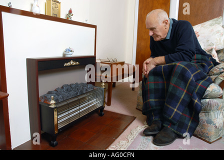 A elderly man sitting infront of his unlit electric fire Stock Photo