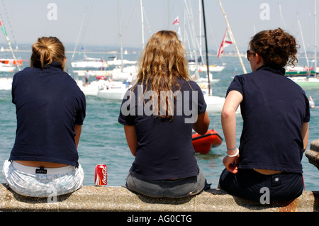 three young ladies girls women sat on the sea wall watching the yacht racing during cowes week on the isle of wight Stock Photo