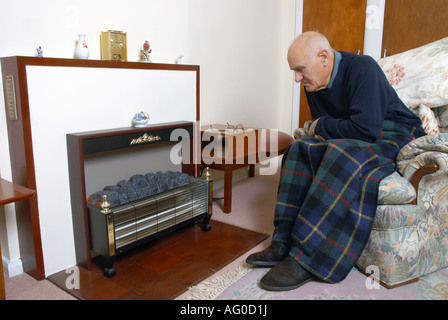 A elderly man sitting infront of his unlit electric fire Stock Photo