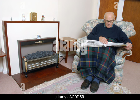 A elderly man sitting infront of his unlit electric fire Stock Photo