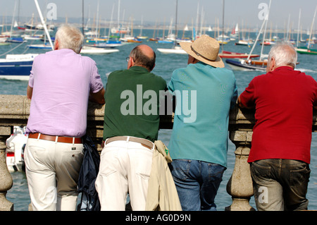 four 4  men leaning on wall chatting during cowes week on the isle of wight Stock Photo
