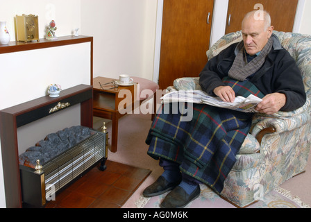 A elderly man sitting infront of his unlit electric fire Stock Photo