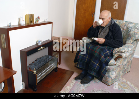 A elderly man sitting infront of his unlit electric fire Stock Photo