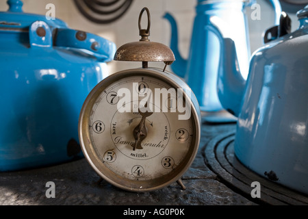 Time for Tea An old antique kitchen timer with a bell on top on a coal stove surrounded by blue kettles Juelsberg Funen Stock Photo