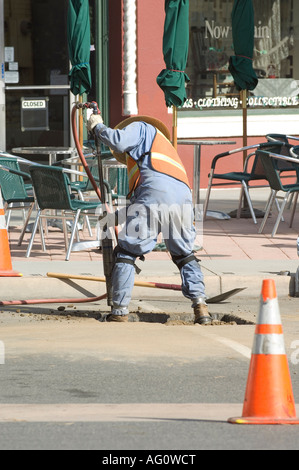 A worker uses a jackhammer to open up a hole in the street. Stock Photo