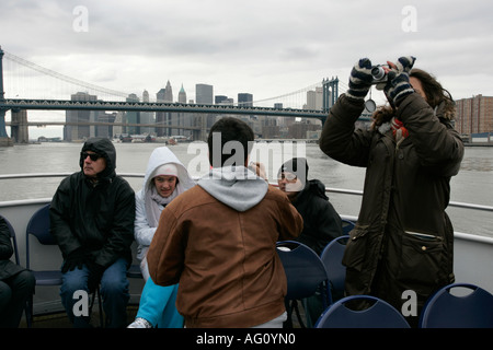 female tourist uses a point and shoot camera with cold tourists on the back of a cruise boat on the east river with new york sky