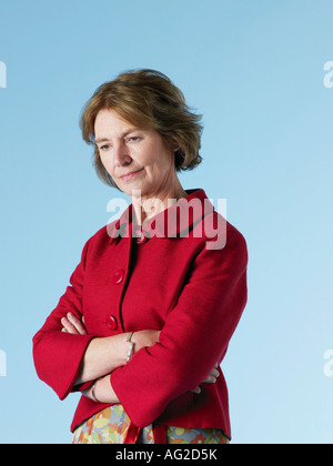 Middle-aged woman on blue background, looking down, arms crossed Stock Photo