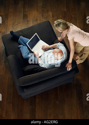 Middle-aged man sitting on sofa using laptop, woman leaning and watching, view from above Stock Photo