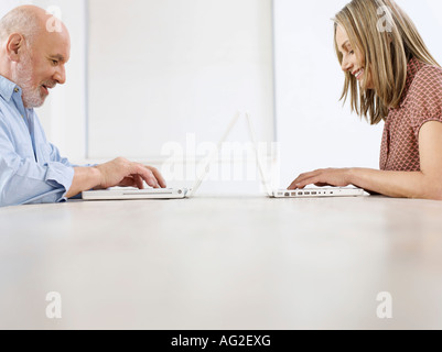 Middle-aged man and mid-adult woman sitting opposite to each other, using laptops, profile Stock Photo