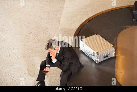 Business man looking at mobile phone sitting on luggage carousel in airport Stock Photo