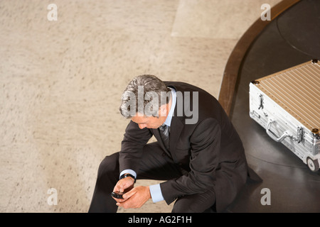 Business man with mobile phone sitting on luggage carousel in airport Stock Photo