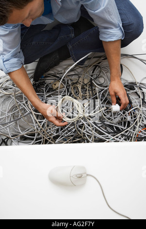 Man working on tangle of computer wires in office Stock Photo
