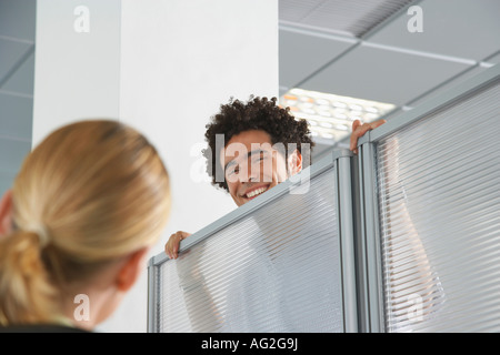 Office worker peering over cubicle wall to greet coworker in office Stock Photo