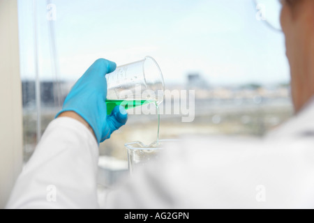 Scientist pouring green liquid in laboratory, focus on hand and beaker Stock Photo