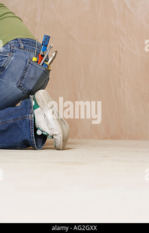 Woman with paintbrush and hand tools in back jeans pocket kneeling on floor, low section Stock Photo