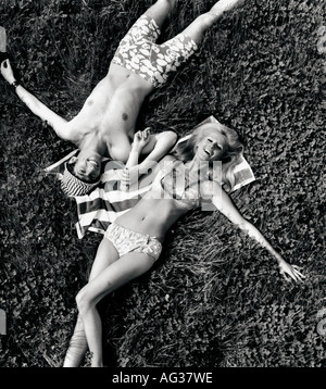 fashion, couple, lying in meadow, full length, 1960s, 60s, bikini, trunks, bathing suit, clothing, two-piece, sunglasses, accessory, Hawaiian, Hawaii, pattern, patterned, flower, flowers, bow, towel,  hat, sun shade, , Stock Photo