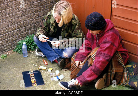 Two young women smoking cannabis and snorting cocaine in a back street. Stock Photo