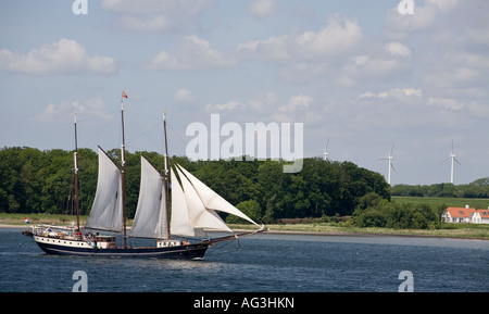 Wind Power A triple masted schooner plys the calm waters between Aero and Funen A row of windmills on shore echo the wind theme Stock Photo