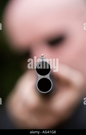 Man pointing a shotgun with the end of the barrel in focus Stock Photo
