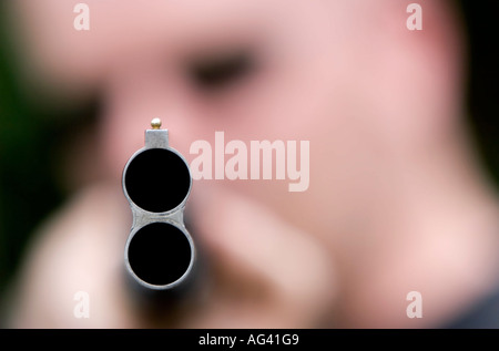 Man pointing a shotgun with the end of the barrel in focus Stock Photo