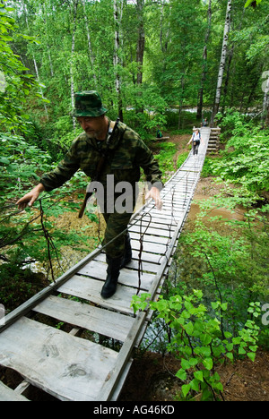 Park ranger with rifle leads hikers across bridge in Baikal Nature Reserve next to Lake Baikal in Siberia Russia Stock Photo