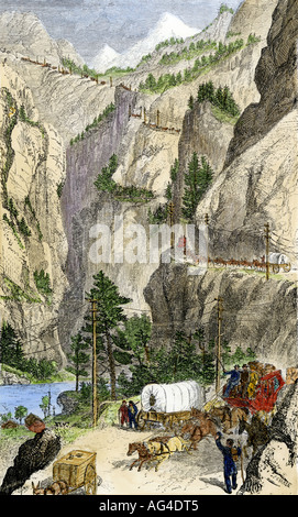 Stagecoaches and covered wagons crossing the Sierra Nevada mountains into California 1865. Hand-colored woodcut Stock Photo