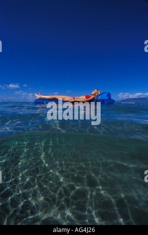 An above and below view of girl floating on a blue mat in Lahaina Maui Stock Photo
