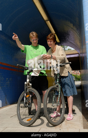 A couple looking at a map on their bikes in an urban town environment Stock Photo