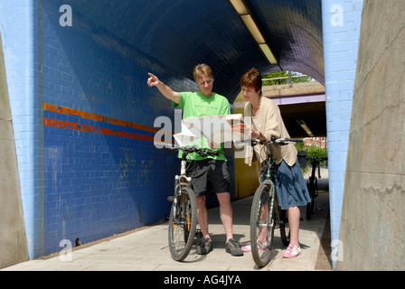 A couple looking at a map on their bikes in an urban town environment Stock Photo